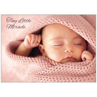 Newborn baby wrapped in pink fabric with 'Tiny Little Miracle' text